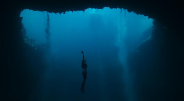Floating in the depths of the ocean, a free-diver stretches her arms towards the surface.