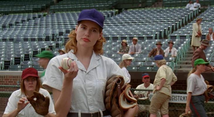 A woman holding a baseball and a baseball glove looks questioningly offscreen.