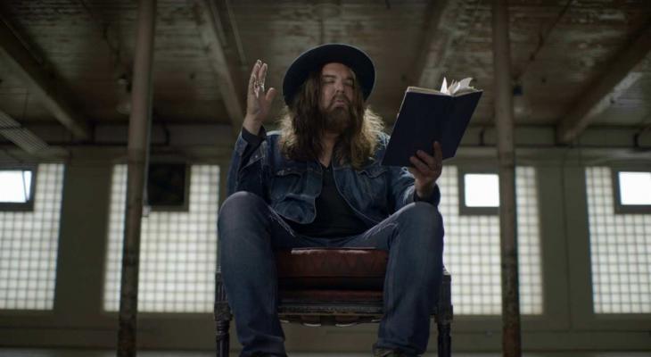 Canadian musician Tom Wilson sits in a chair reading aloud from a journal.