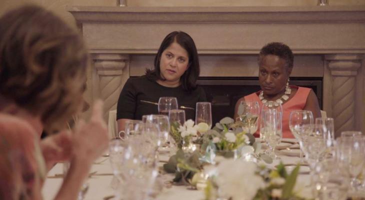 Two women sit at the end of an elaborately set dinner table. 