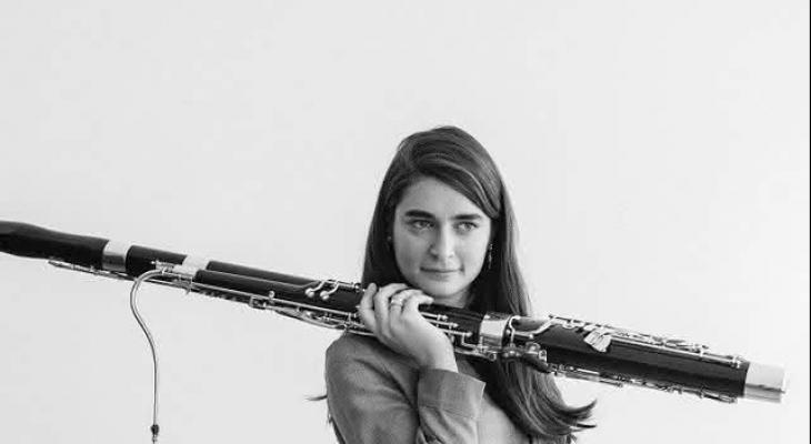 Black and white image of Sophie Dervaux, a woman with long, dark hair, holding a bassoon over her shoulder.