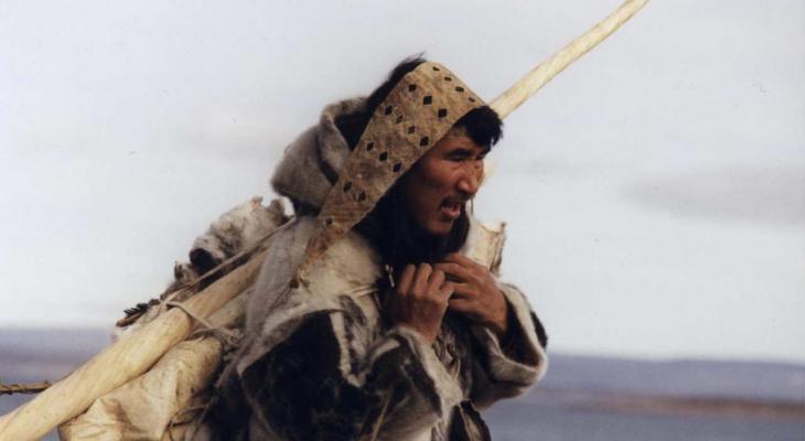 A man walking across a broad landscape laden down with belongings.