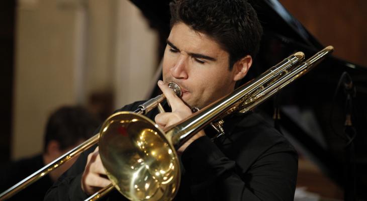 Fabrice Millischer plays his trombone in recital, standing in front of a grand piano.