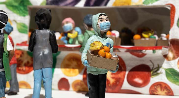 Polymer clay figures at a food bank. The figure in the foreground in holding a box with groceries and wearing a blue mask.