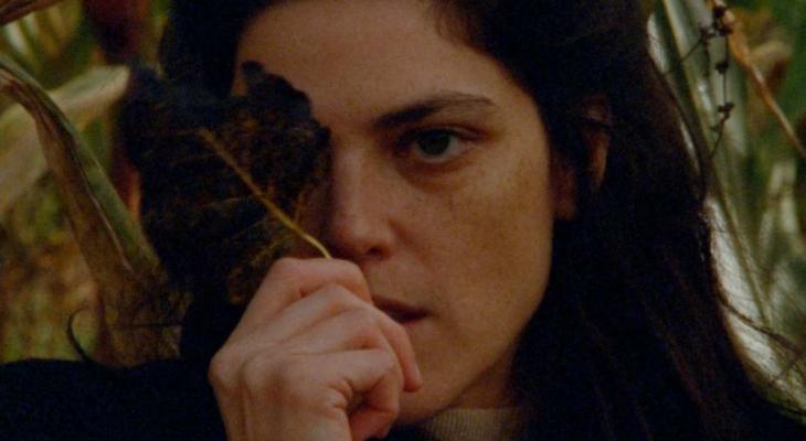 a woman holding a leaf over her left eye