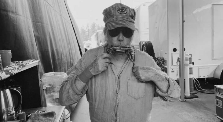 Neil Young with a striped cap and sunglasses playing harmonica