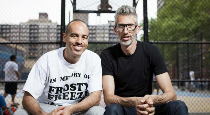 DJs Stretch and Bobbito smile for the camera outside a basketball court.