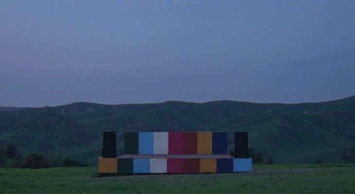 a multi-coloured stage in the middle of a field with mountains in the background