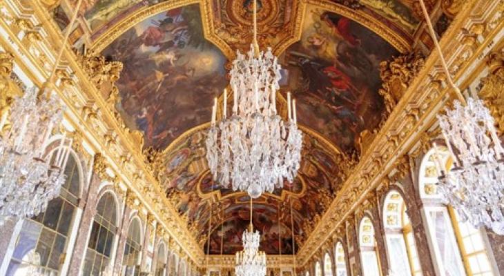 Hall of Mirrors at the Palace of Versailles during the day, featuring ornate painting ceiling, and grand chandeliers. 