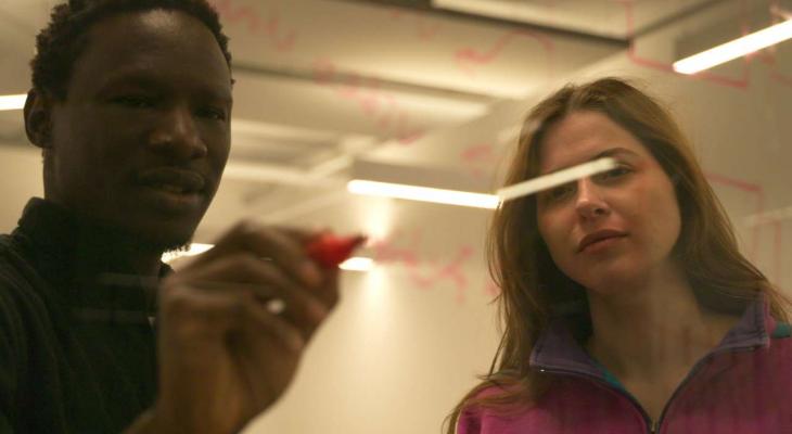 A man and a woman look at calculations on a board.