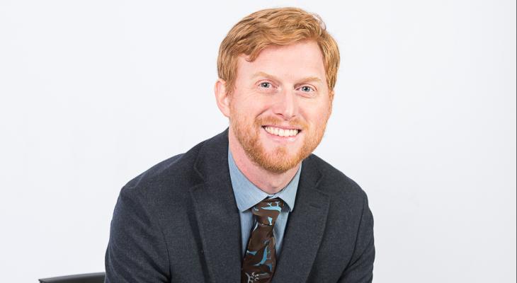 Prof. adam patrick bell, in front of a white background, smiles and faces the camera