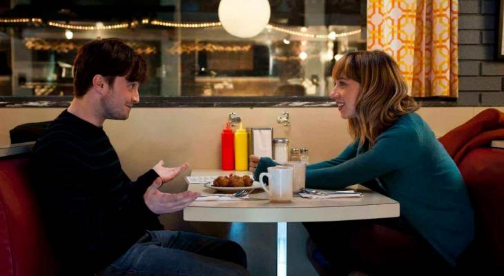 A young man and woman have a conversation at a booth in a diner.
