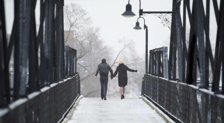 Holding hands, a man and a woman cross a bridge in the snow.