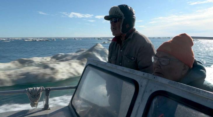 Two men drive a boat in the Arctic.