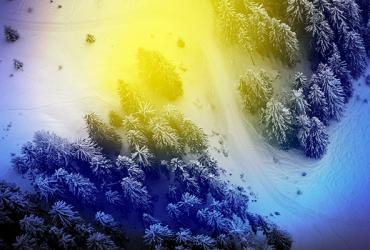 An aerial view of a field and evergreens covered with snow with a blue and yellow aura filter.