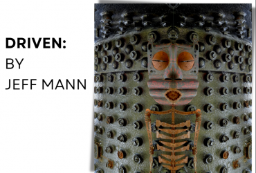 A photograph of an art piece made of old car parts, with a person painted on top.