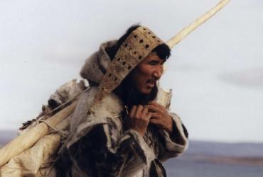 A man walking across a broad landscape laden down with belongings.