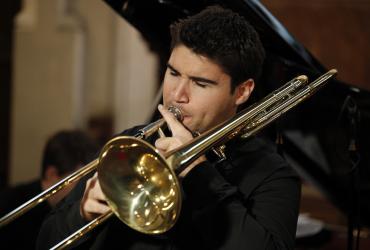 Fabrice Millischer plays his trombone in recital, standing in front of a grand piano.