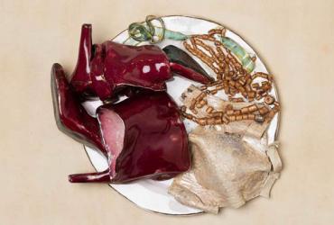 A ceramic sculpture of a dinner plate with red boots, a nude bra, a necklace, and other accessories