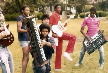 a group of people playing with guitars and synthesizers in a park