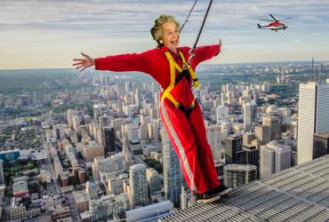 Photoshopped image of an elderly woman leaning out over the edge of the CN tower in a red bodysuit. 