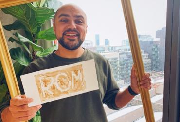 Portrait of host Kiron holding a sign that reads ROM