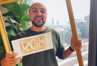 Portrait of host Kiron holding a sign that reads ROM