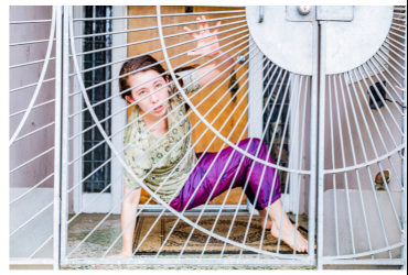 Photograph of a person crouched behind a gate. The gate has straight and curved lines running across it. With text: Something Heroic and Distant: Dancers Creating in the time of COVID-19. Photography by Kyle Adler, Jan 4-31