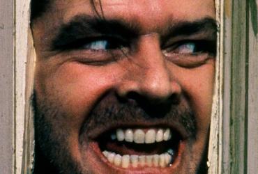 Jack Torrance (Jack Nicholson) aggressively pushes his face through a broken door.