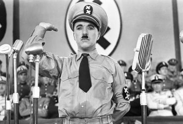 Charlie Chaplin in a military uniform saluting in front of microphones