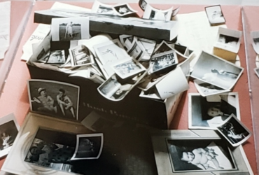 A collection of black and white photographs scattered around and inside a shoebox. With text: The Shoebox Collection, photographs by irving fistell.