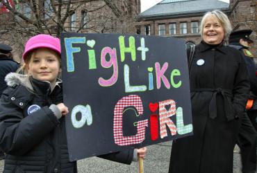 a girl and a woman hold a sign at a protest that says fight like a girl