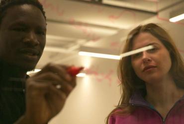 A man and a woman look at calculations on a board.