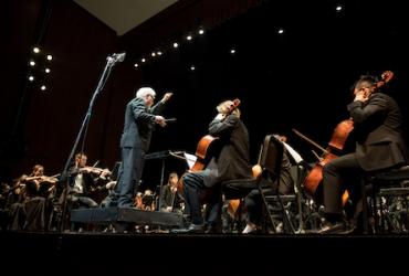 This picture shows a scene of a band rehearsing, with musicians gathered around the conductor in the middle of the stage.