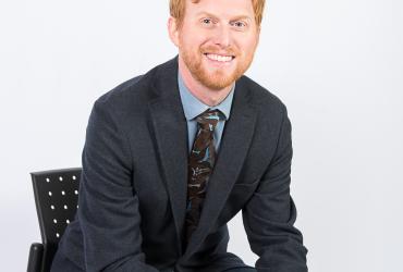 Prof. adam patrick bell, in front of a white background, smiles and faces the camera