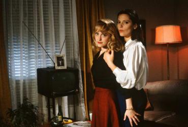 Two lesbians embrace in a 1950s-style Canadian living room.