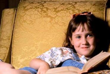 Matilda sits in an armchair reading a book.