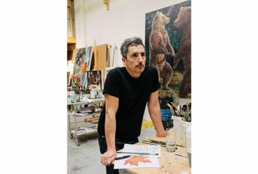 Artist Kent Monkman standing at a table in his studio.
