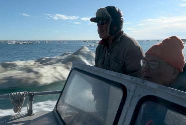 Two men drive a boat in the Arctic.